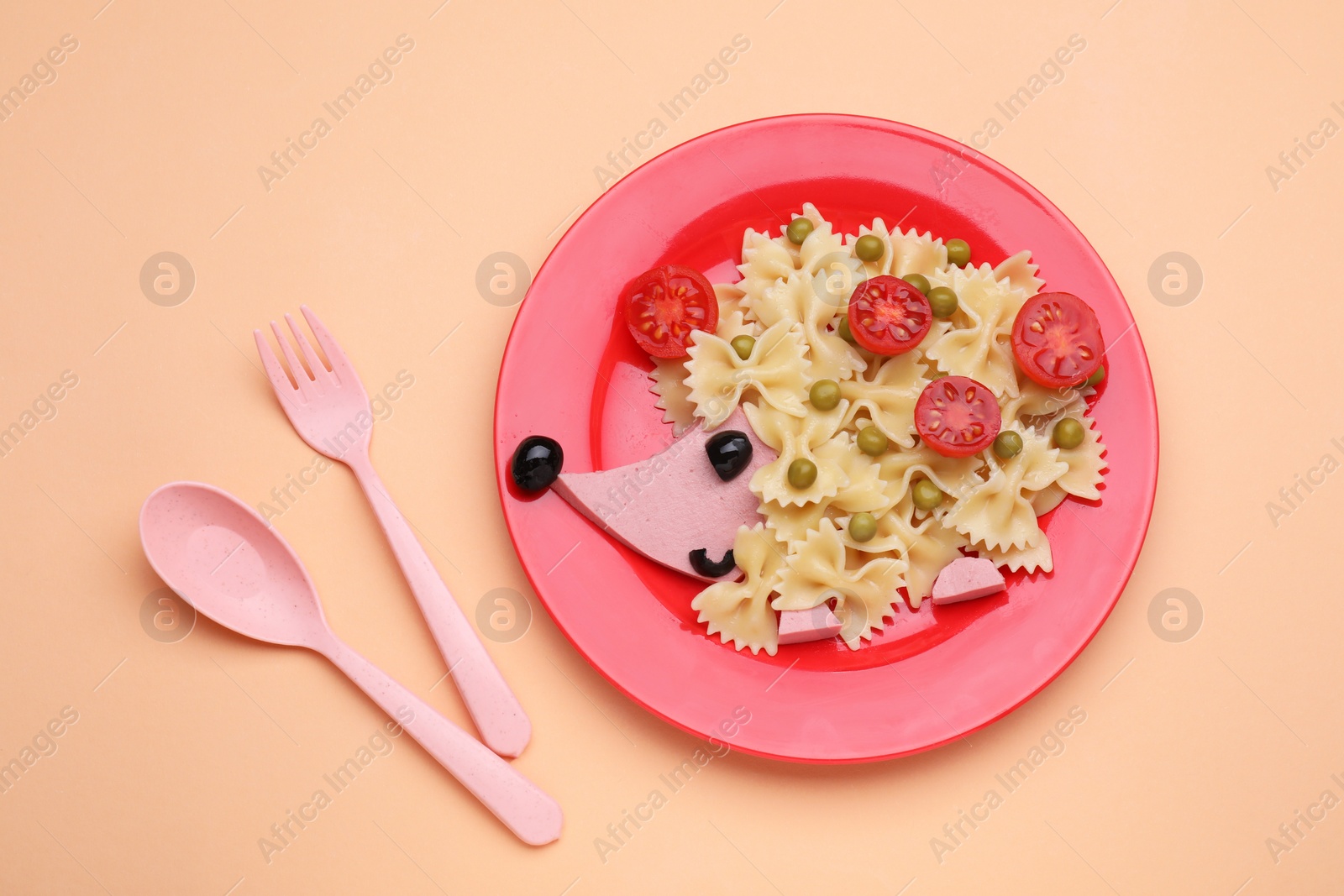 Photo of Plate with cute hedgehog made of delicious pasta, sausages and tomatoes on pale orange table, flat lay. Creative serving for kids