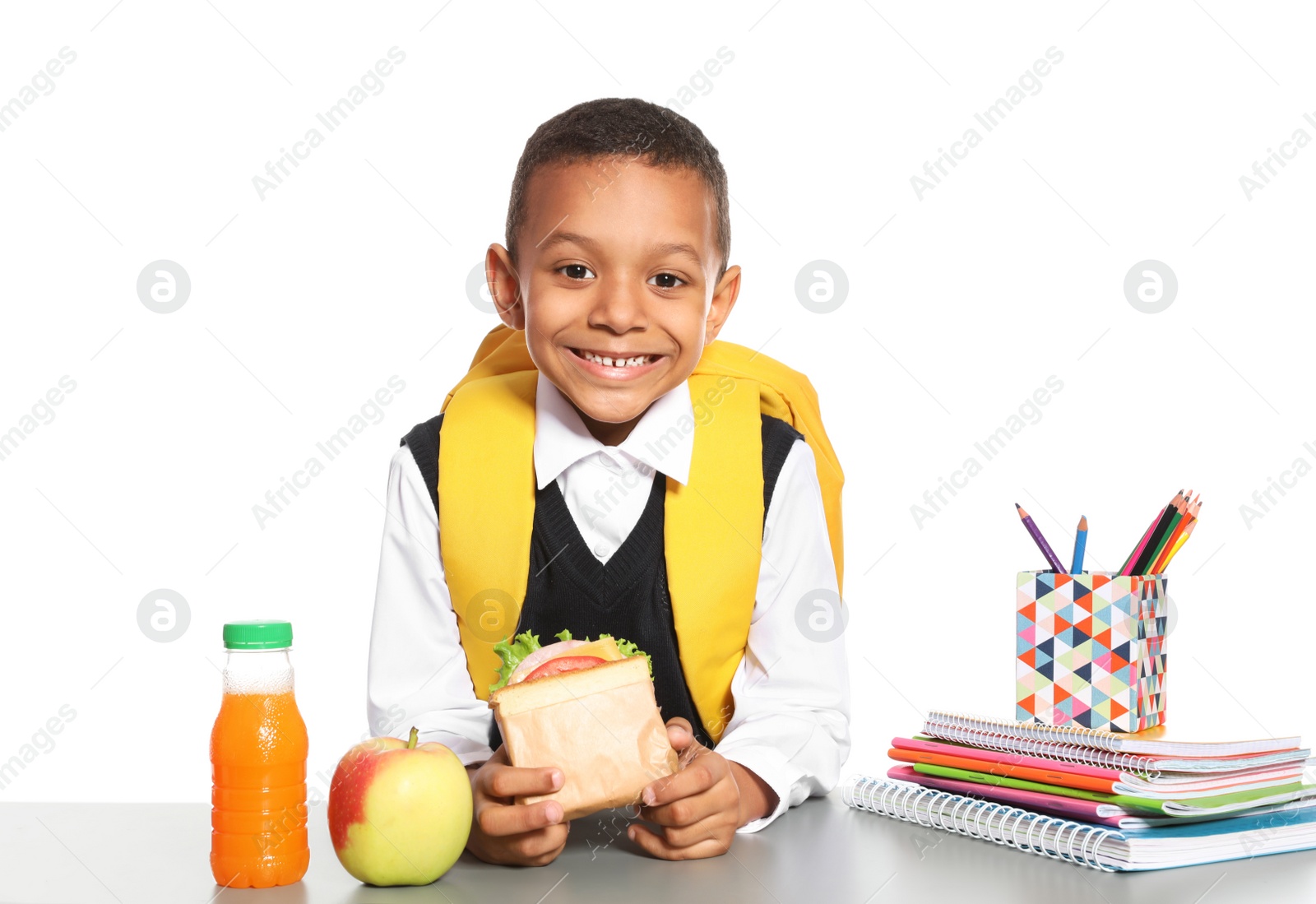 Photo of African-American schoolboy with healthy food and backpack sitting at table on white background