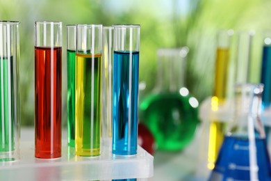 Photo of Test tubes with liquids in stand against blurred background, closeup