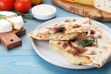 Photo of Tasty pizza calzones with cheese and different products on light blue wooden table, closeup