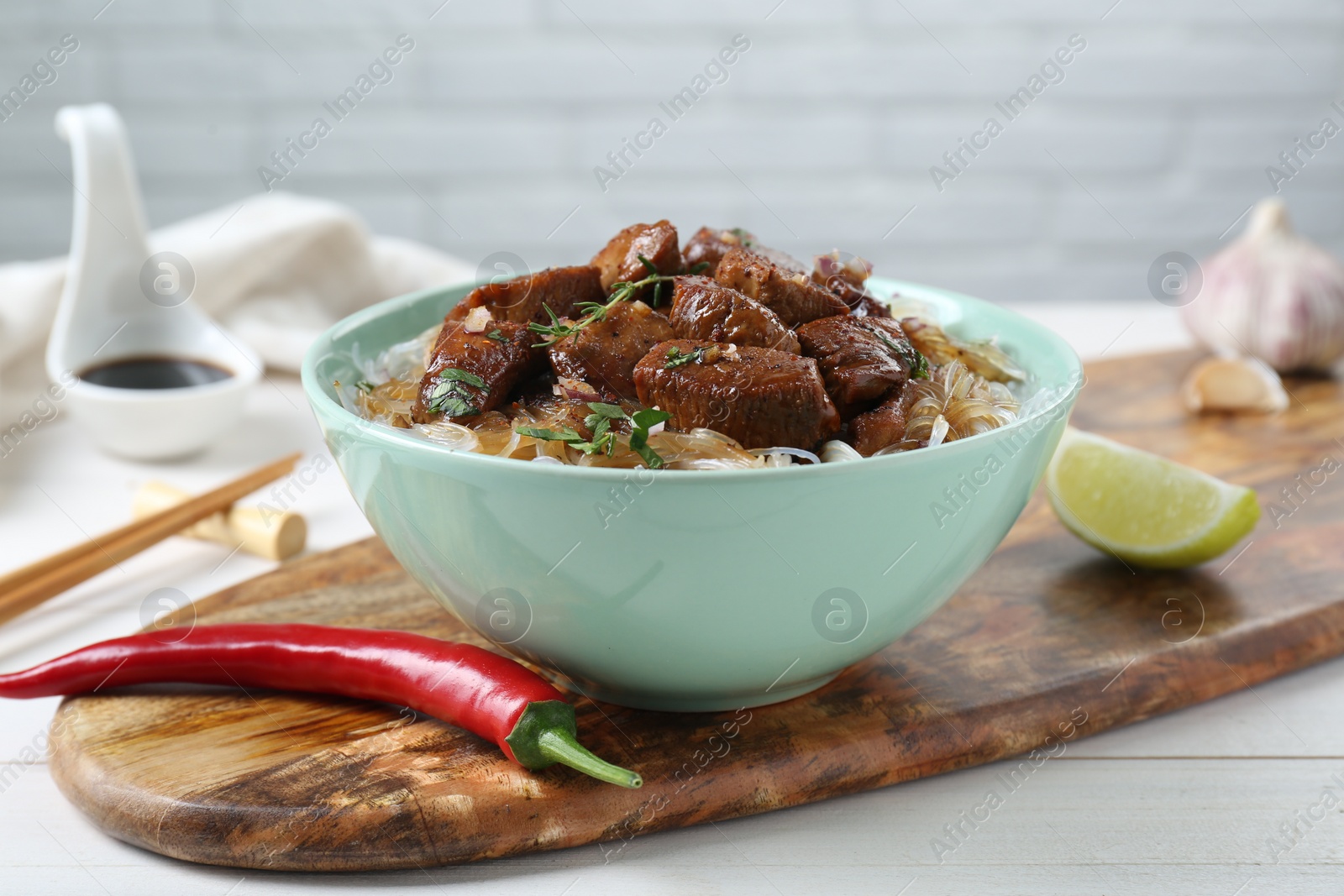Photo of Bowl with pieces of soy sauce chicken and noodle on white table
