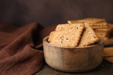 Photo of Cereal crackers with flax and sesame seeds in bowl on wooden table, closeup. Space for text