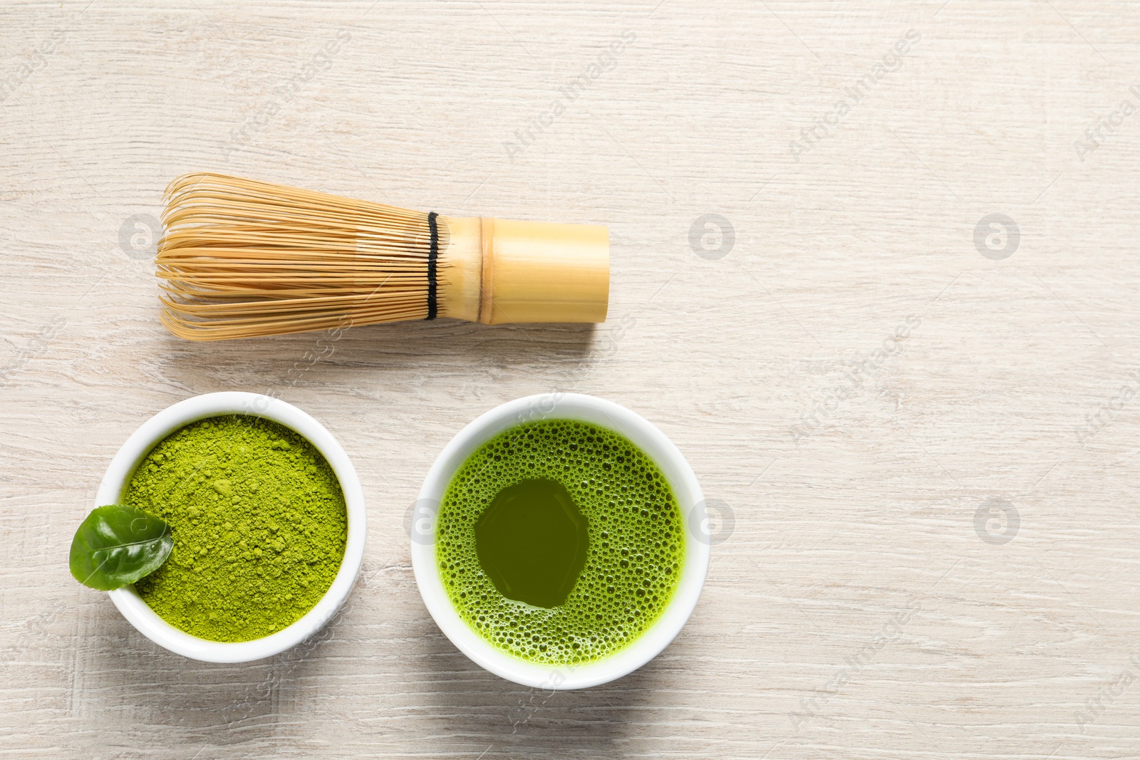 Photo of Cup of fresh matcha tea, bamboo whisk and green powder on wooden table, flat lay. Space for text