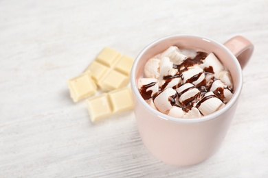 Photo of Cup of chocolate milk with marshmallows on light wooden background