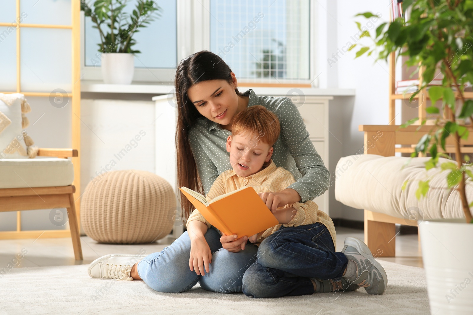 Photo of Mother reading book with her son on floor in living room at home