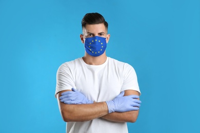 Man wearing medical mask with European Union flag on light blue background. Coronavirus outbreak in Europe
