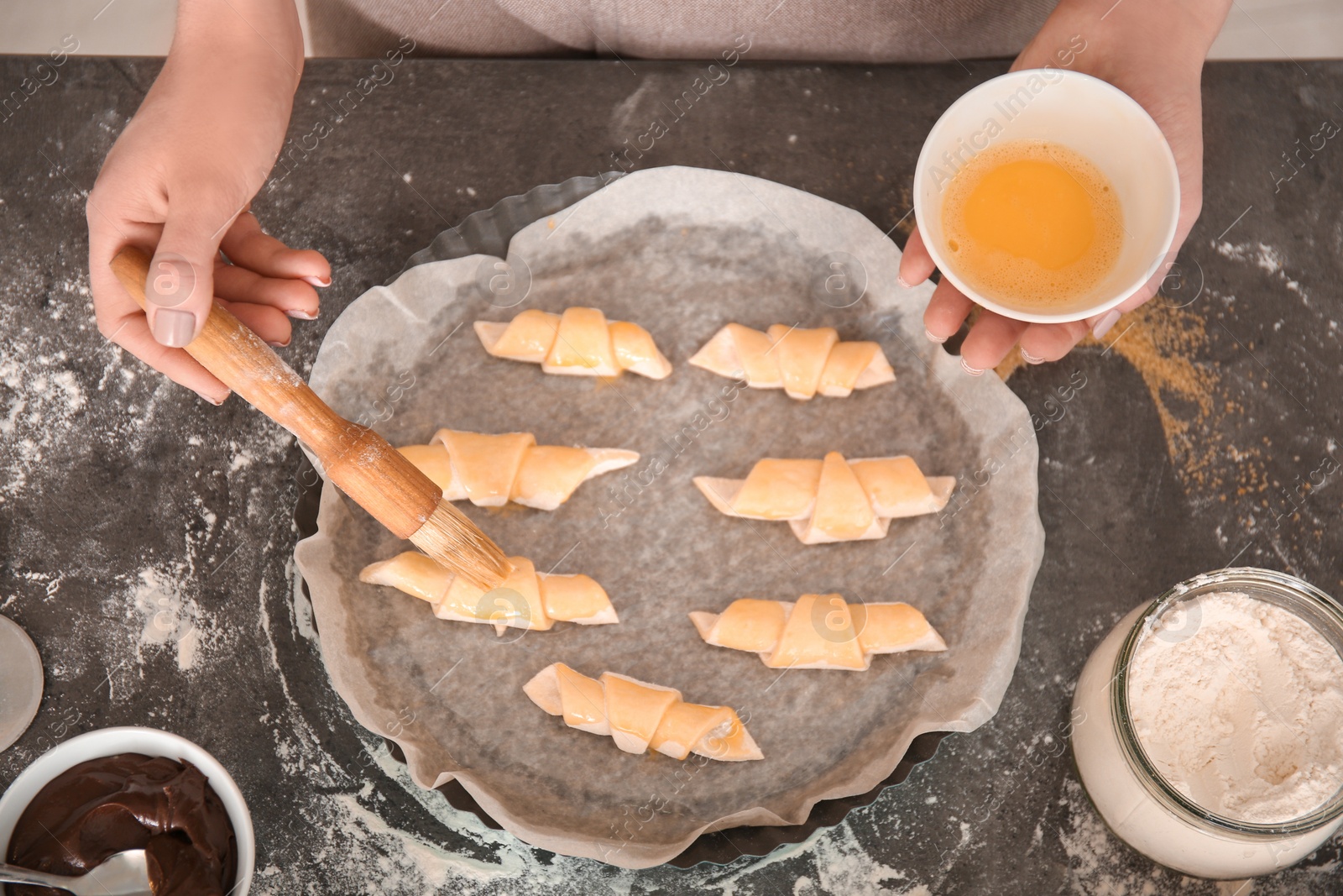 Photo of Woman spreading egg yolk on croissants, top view