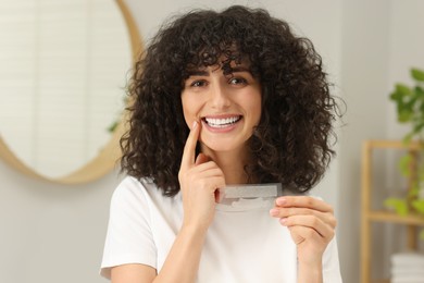 Young woman holding teeth whitening strips in bathroom