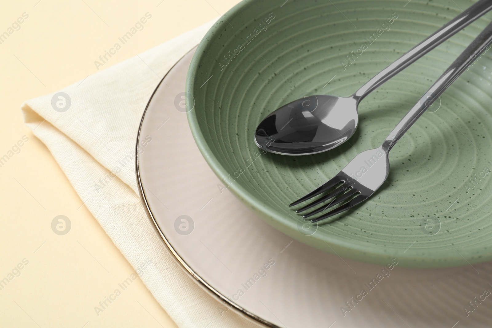 Photo of Stylish ceramic plate, bowl, cutlery and napkin on beige background, closeup