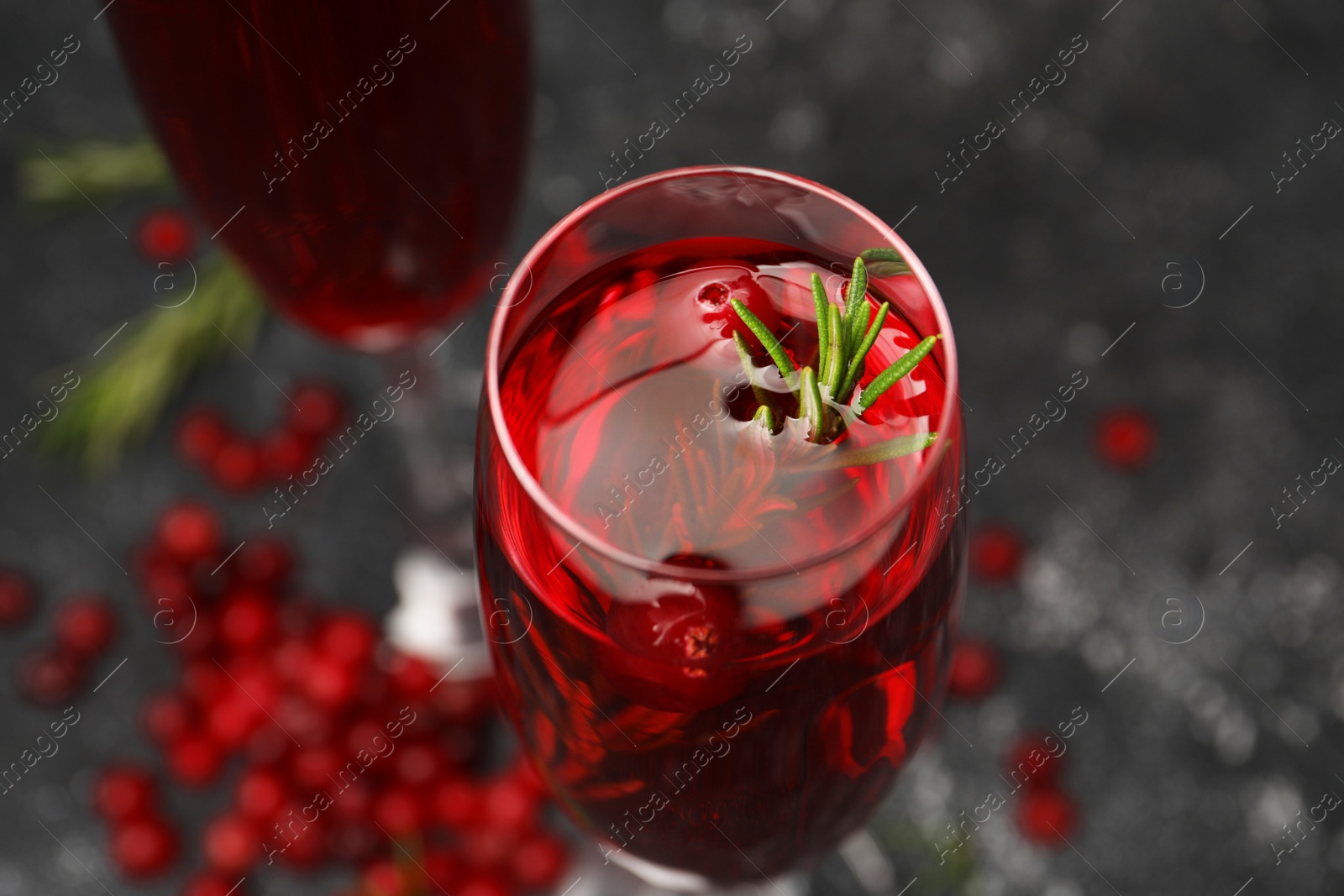Photo of Tasty cranberry cocktail with rosemary in glass on gray table, closeup