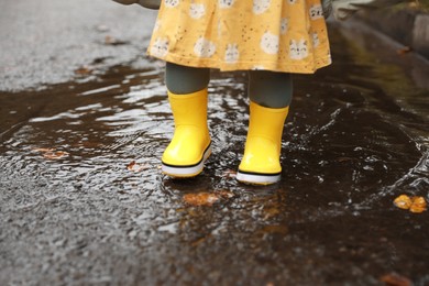 Little girl wearing yellow rubber boots standing in puddle outdoors, closeup