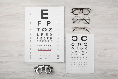 Photo of Vision test chart, glasses and trial frame on light wooden background, flat lay