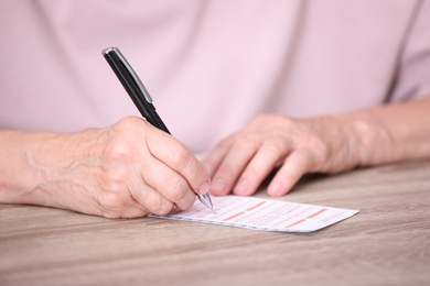 Senior woman filling out lottery ticket at table, closeup