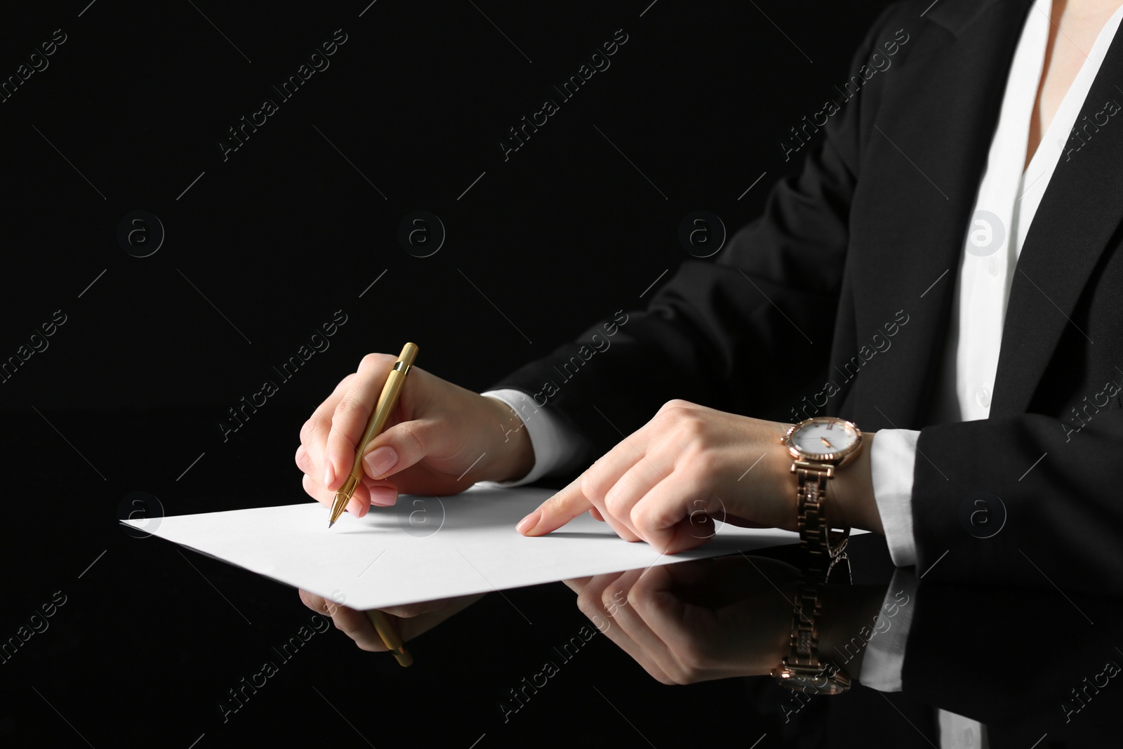 Photo of Woman writing on sheet of paper at glass table, closeup