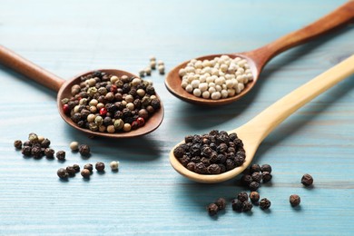 Aromatic spice. Different peppers in spoons on light blue wooden table, closeup