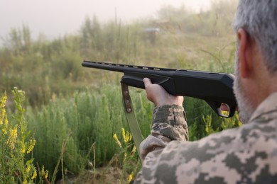 Photo of Man wearing camouflage and aiming with hunting rifle outdoors, closeup