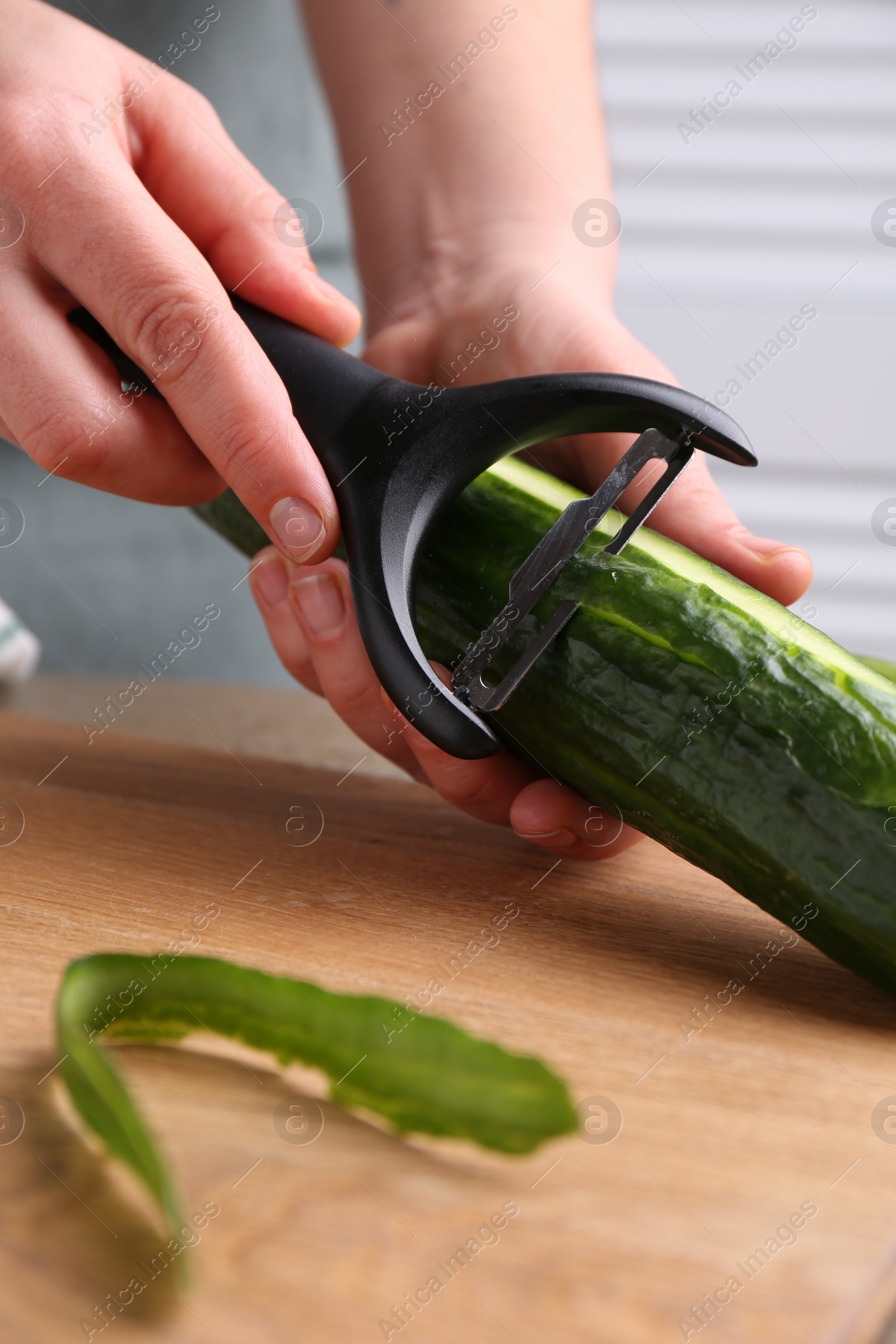 Photo of Woman peeling cucumber at wooden table indoors, closeup