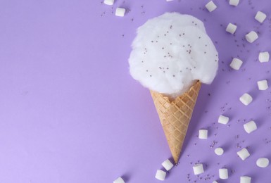 Photo of Sweet cotton candy in waffle cone and marshmallows on purple background, flat lay. Space for text