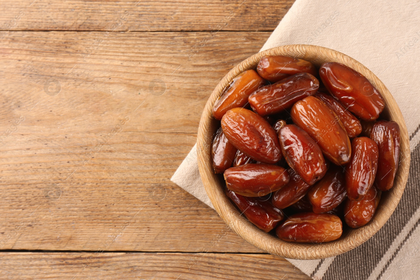 Photo of Sweet dried dates in bowl on wooden background, top view. Space for text