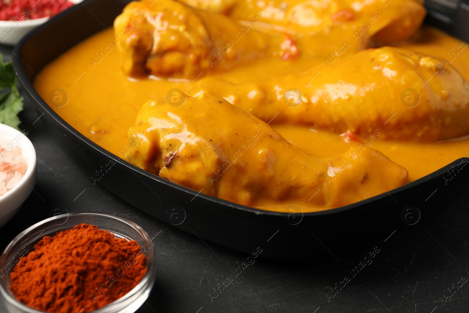 Photo of Tasty chicken curry and ingredients on black table, closeup