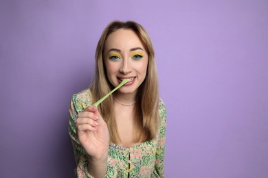 Photo of Fashionable young woman with bright makeup chewing bubblegum on lilac background