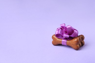 Photo of Bone shaped dog cookies with beautiful bow on purple background, space for text