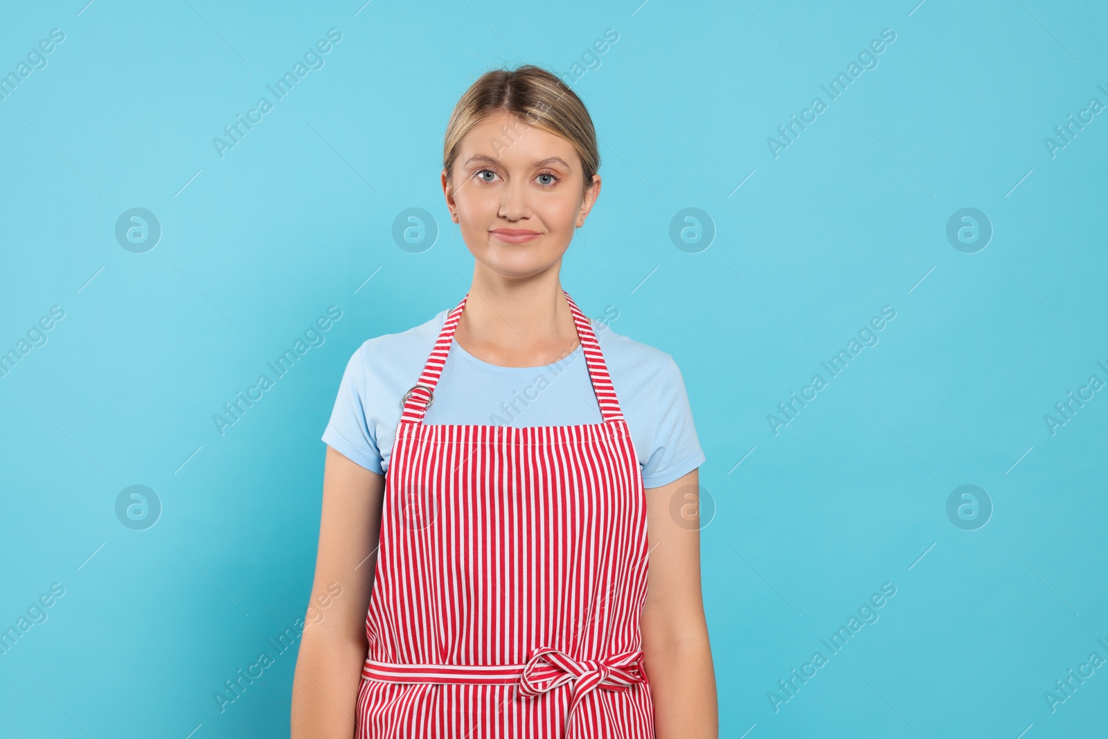 Photo of Beautiful young woman in clean striped apron on light blue background