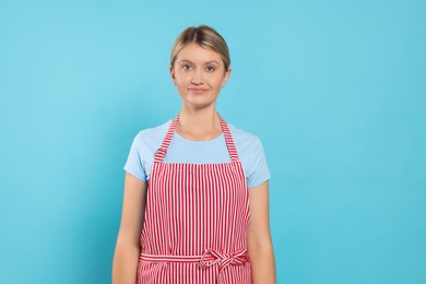 Beautiful young woman in clean striped apron on light blue background