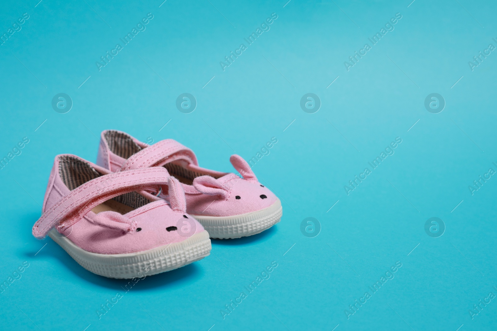 Photo of Cute baby shoes on light blue background, space for text