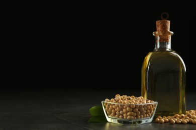 Photo of Glass bottle of oil, leaves and soybeans on grey table. Space for text