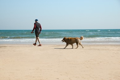 Photo of Man walking his dog on sea beach