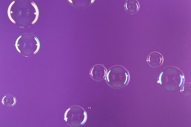 Photo of Beautiful transparent soap bubbles on violet background