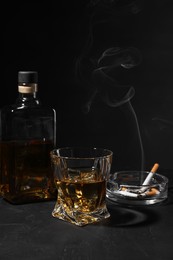 Photo of Alcohol addiction. Whiskey, smoldering cigarettes and ashtray on dark textured table
