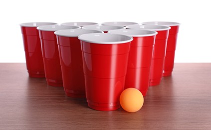 Photo of Plastic cups and ball for beer pong on wooden table against white background