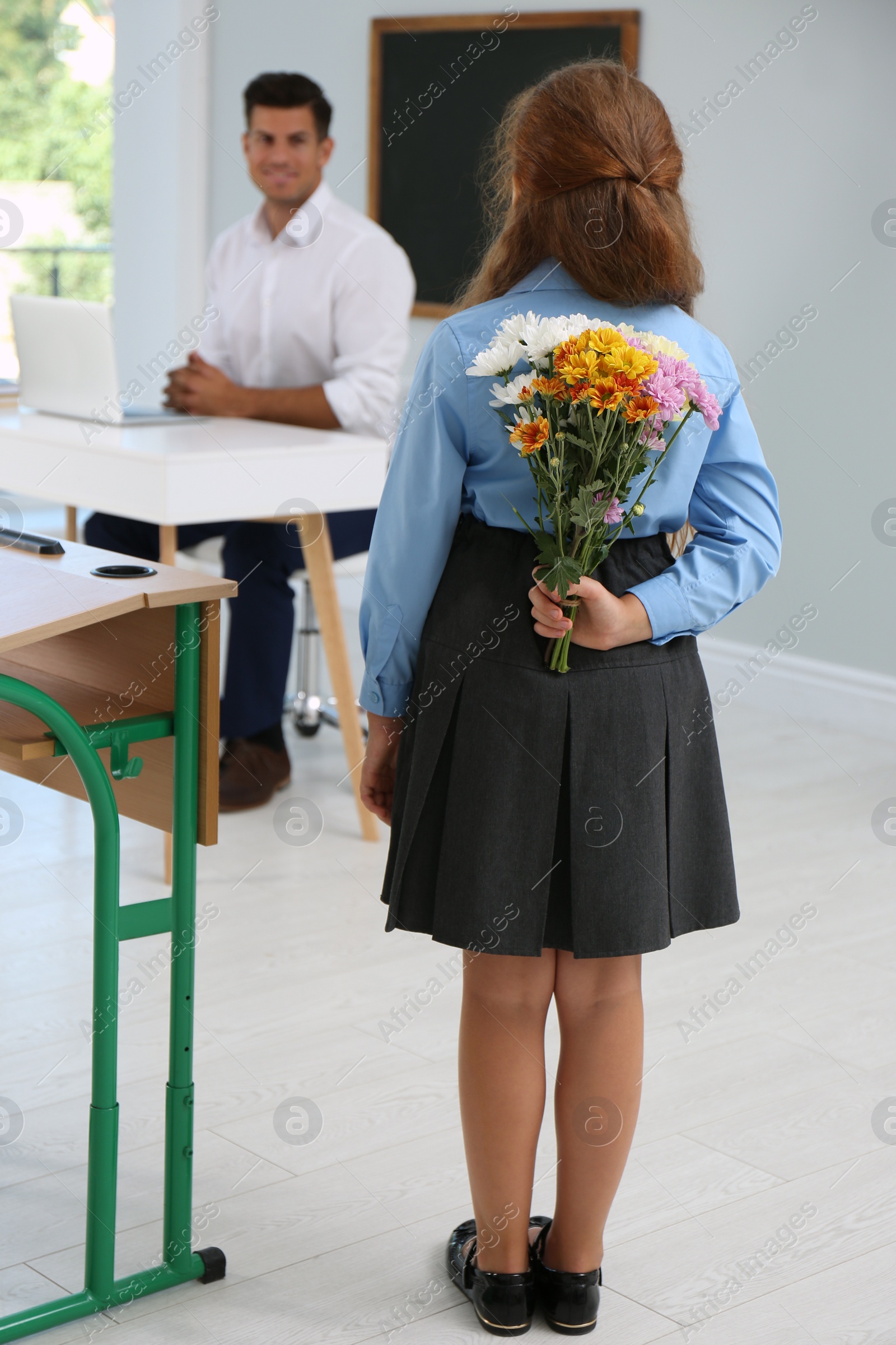 Photo of Schoolgirl with bouquet congratulating her pedagogue in classroom. Teacher's day