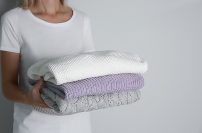 Woman with stack of knitted sweaters on grey background, closeup