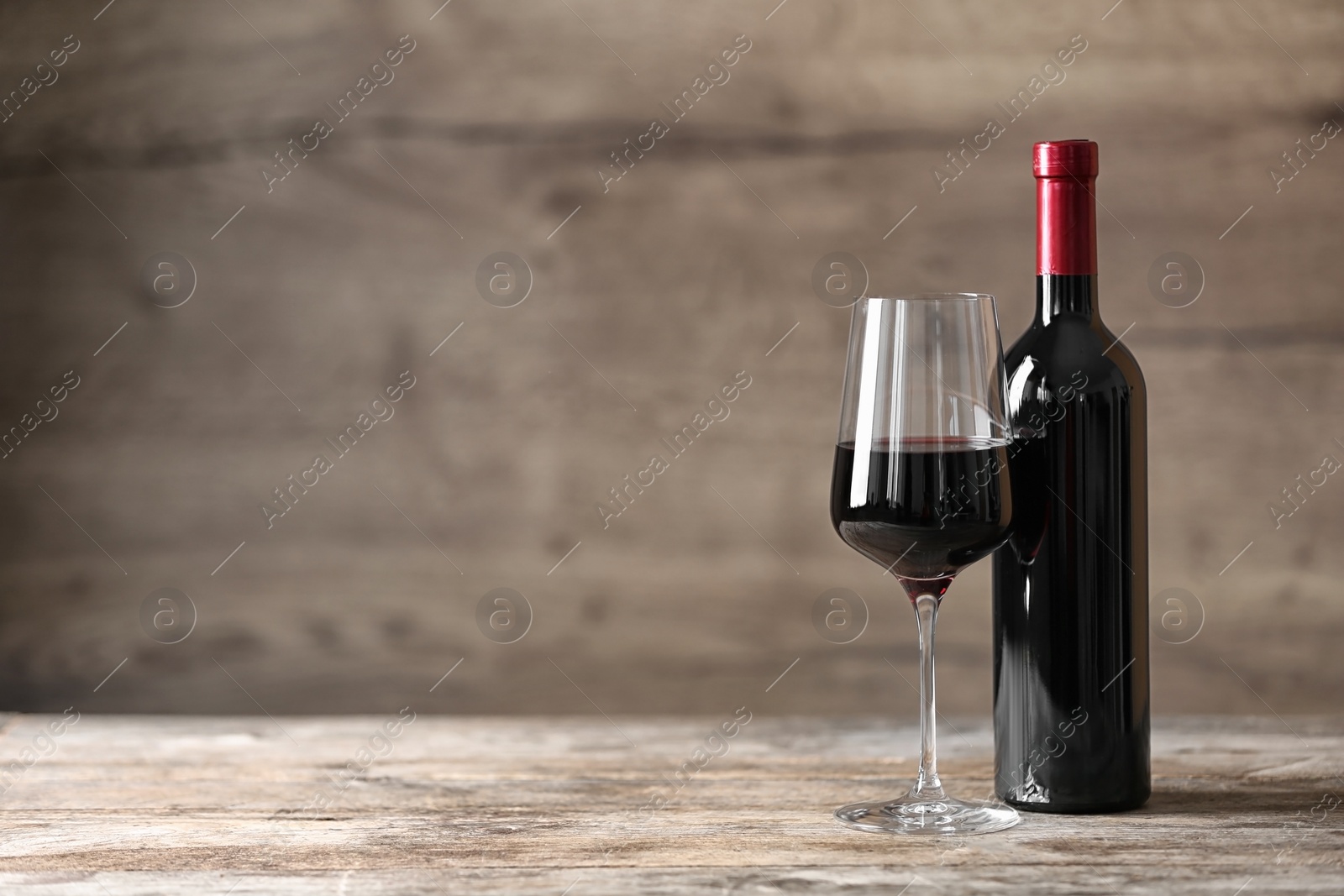 Photo of Glass and bottle of red wine on wooden table. Space for text