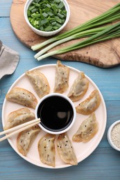Photo of Delicious gyoza (asian dumplings) with green onions and soy sauce served on light blue wooden table, flat lay