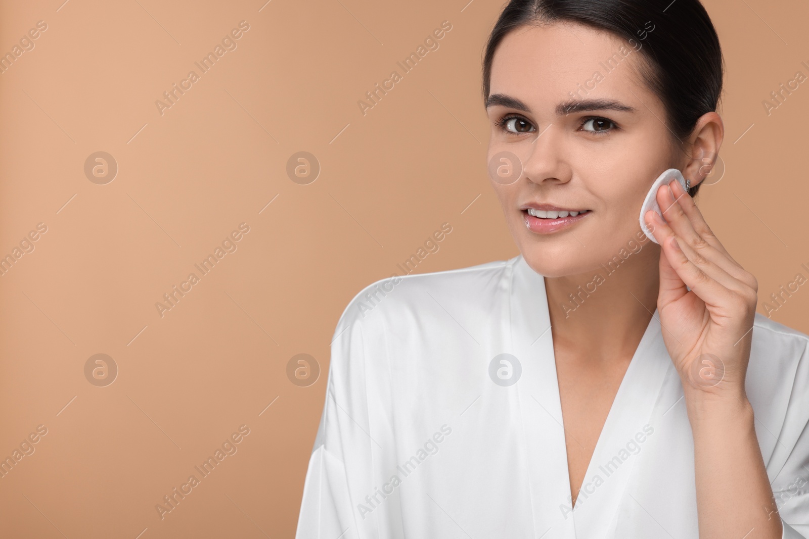 Photo of Young woman cleaning her face with cotton pad on beige background. Space for text