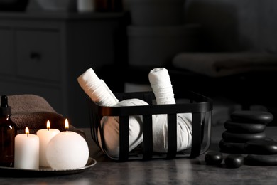Photo of Herbal massage bags, burning candles and stones on grey table. Spa products