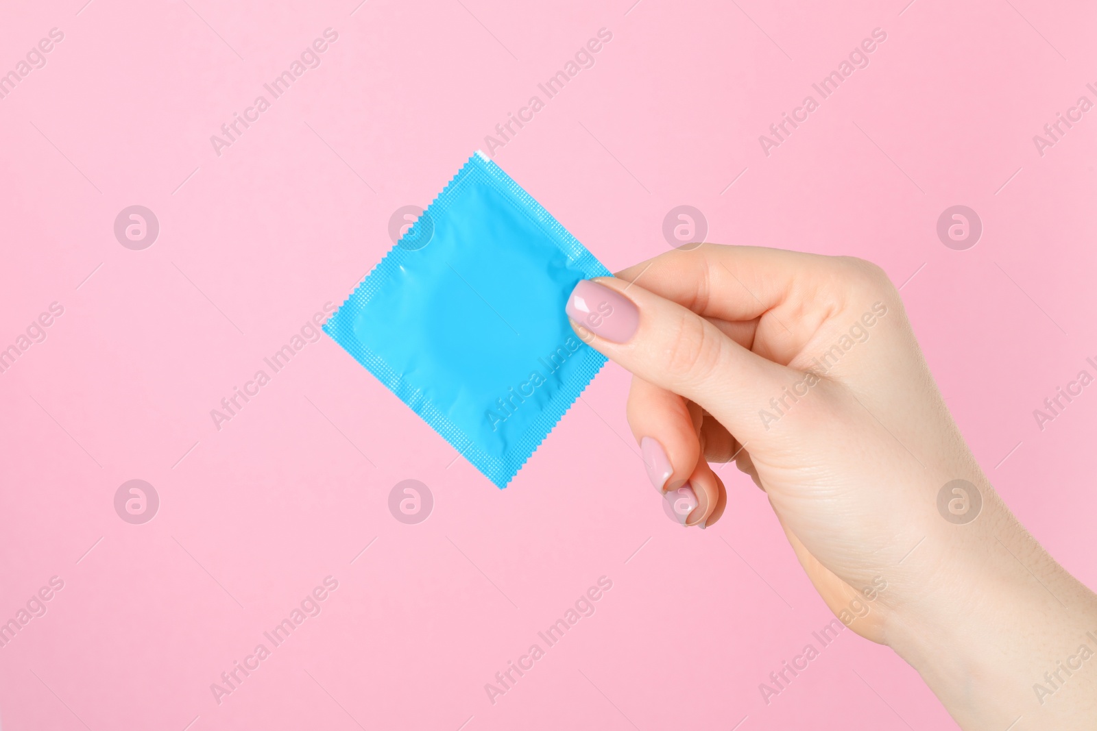 Photo of Woman holding condom on pink background, closeup