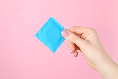 Woman holding condom on pink background, closeup