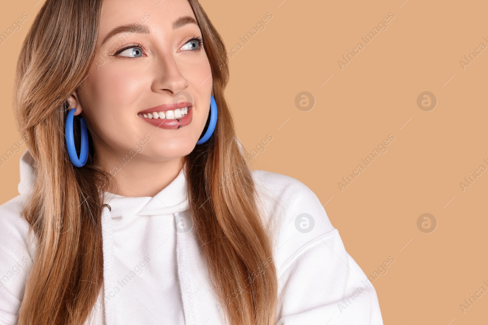 Photo of Young woman with lip piercing on beige background. Space for text