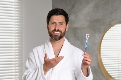 Happy man with tongue cleaner in bathroom
