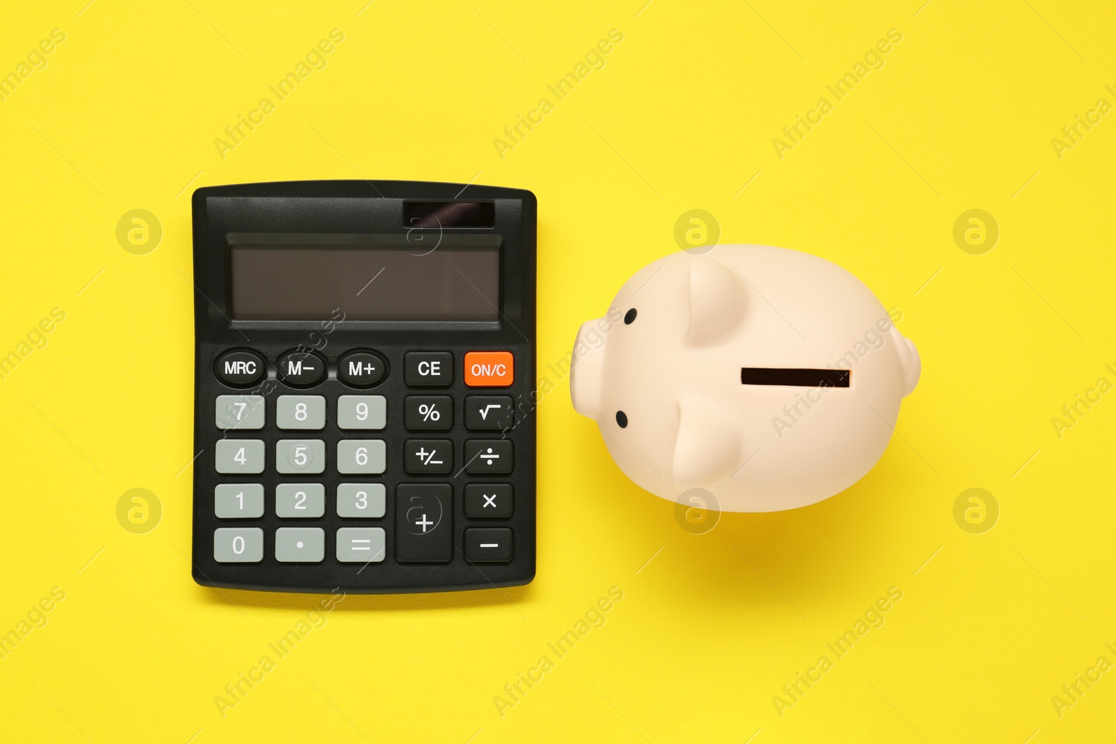 Photo of Calculator and piggy bank on yellow background, top view