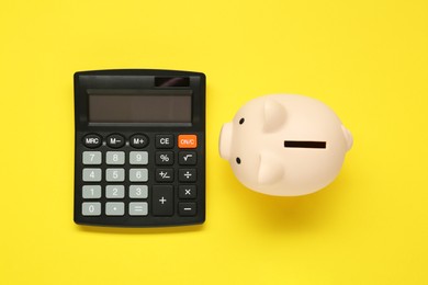 Calculator and piggy bank on yellow background, top view