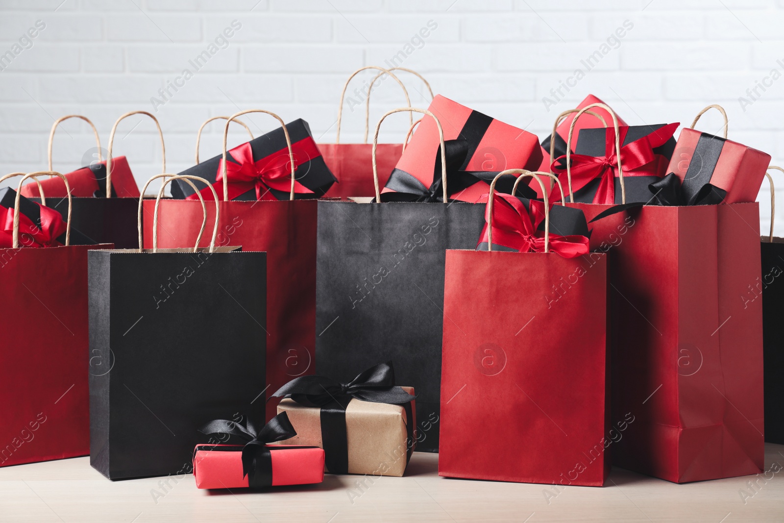 Photo of Paper shopping bags and gift boxes on table near white brick wall. Black Friday sale