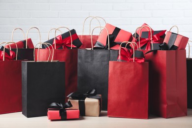 Photo of Paper shopping bags and gift boxes on table near white brick wall. Black Friday sale