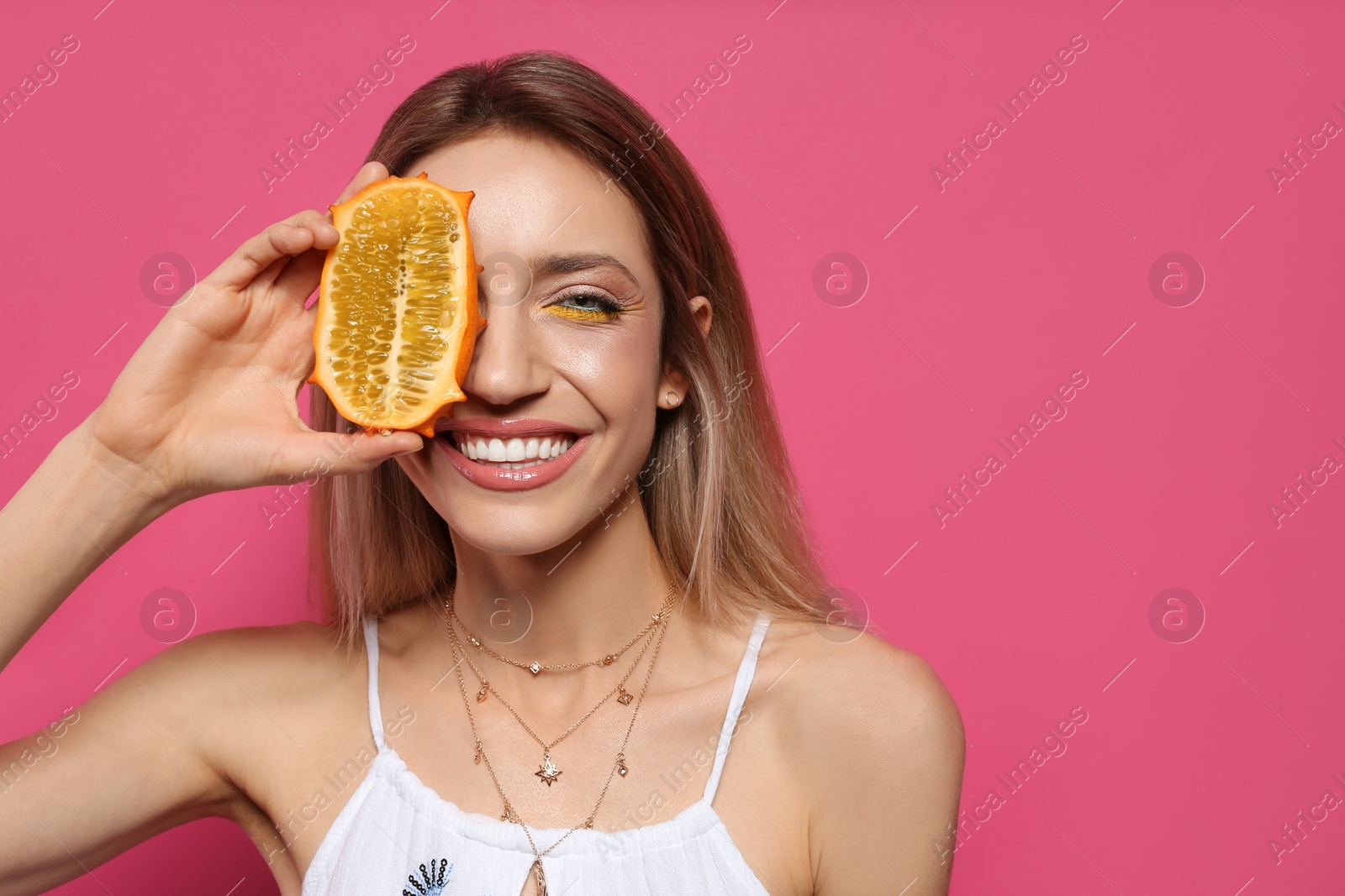 Photo of Young woman with fresh kiwano on pink background, space for text. Exotic fruit