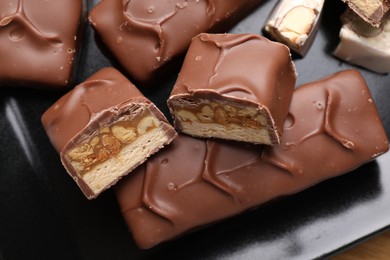 Photo of Tasty chocolate bars with nougat and nuts on black plate, closeup